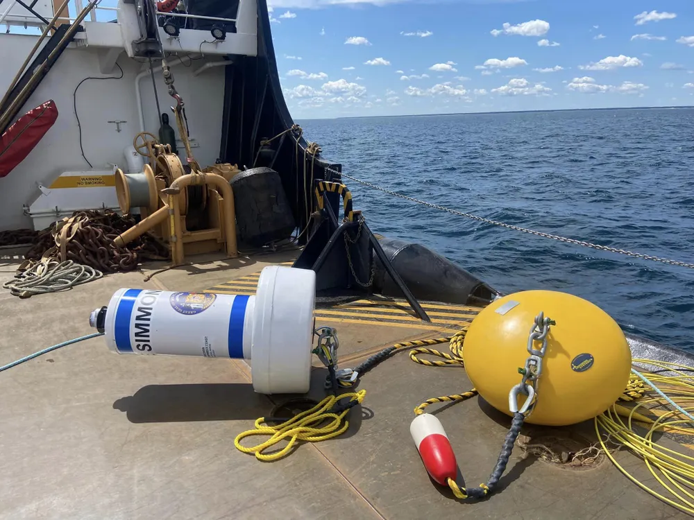 A white buoy attached to a yellow circular-shaped object next to water