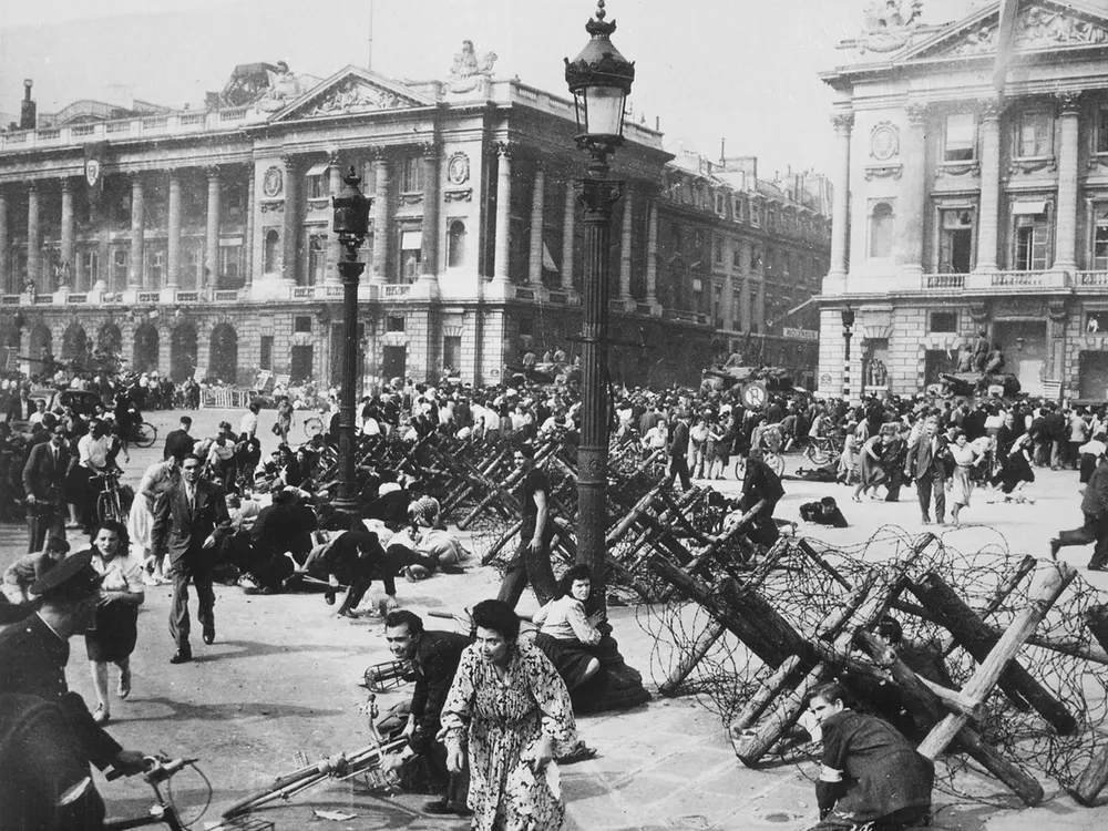 Crowds of Parisians celebrating the entry of Allied troops into Paris scatter for cover as a sniper fires from a building on the Place de la Concorde.