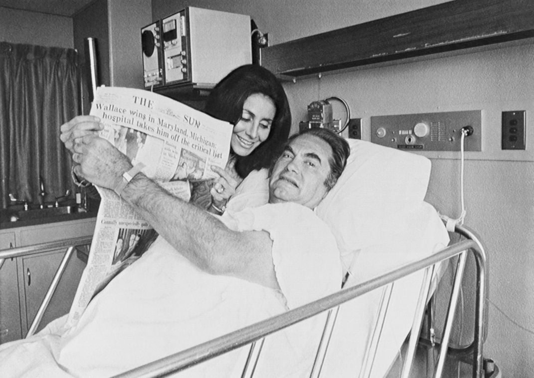 After his shooting, a hospitalized Wallace holds up a newspaper touting his victories in the Maryland and Michigan Democratic presidential primaries.