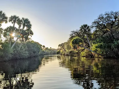 Trees line a winding river, and the blue sky is reflected in the water