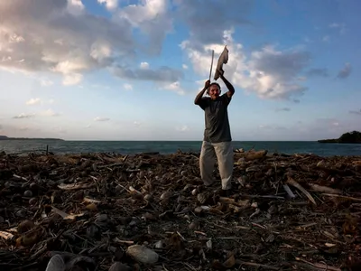 Taíno cacique Francisco Ramírez Rojas beats a palm frond to drive away bad spirits at a seaside ceremony of thanksgiving. A three-sided idol known as La Muñequina is thought to represent the Taíno belief that spirits of the dead are present among the living.