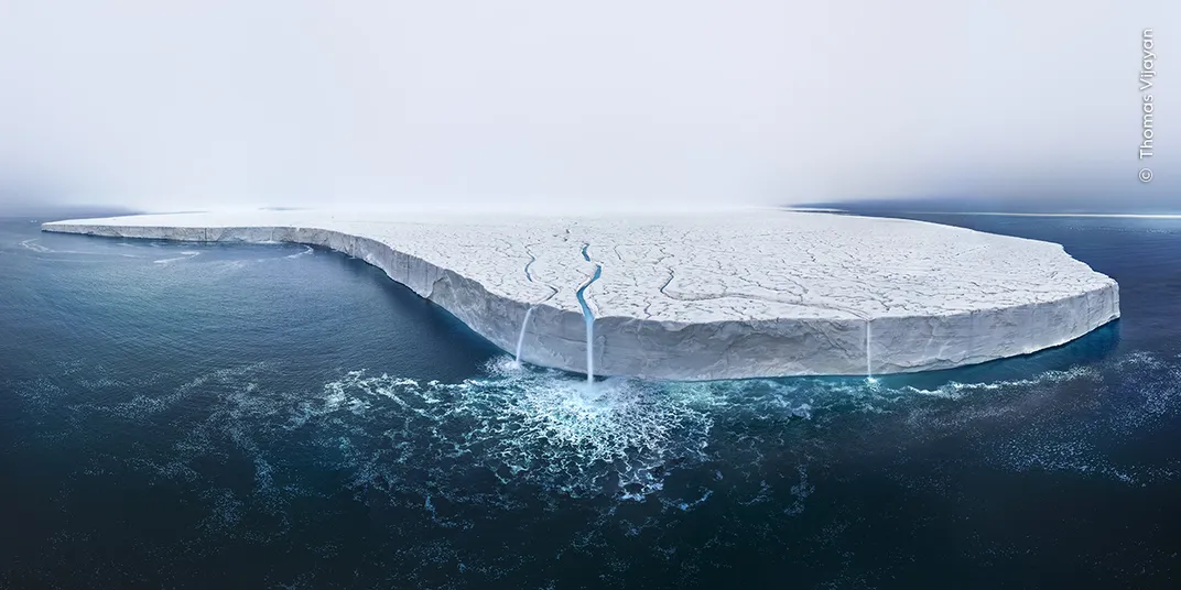 a zoomed-out image of a floating glacier, with a few streams of water trickling off its edge